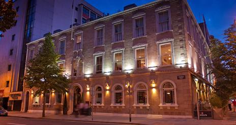 Exterior view of a three-story city hotel, lit at night with a tree.