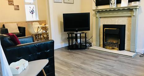 A living room with a fireplace, chair and TV leading to a dining area.