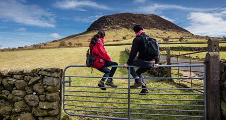 A couple of hikers sitting on a gate admiring the view of Slemish in the background