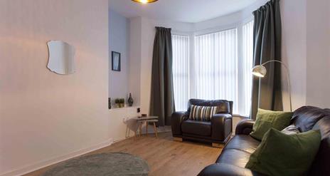 A living room with a leather sofa, armchair, and a bay window with blinds and curtains.