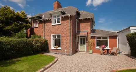 exterior of a semidetached cottage with a stone driveway, a lawn and some garden furniture.