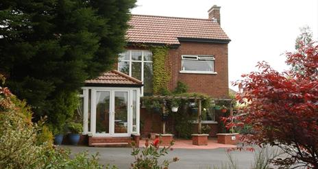 A B&B seen through a colourful garden of trees, bushes and flowers.