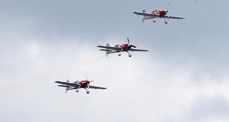 three red and white planes flying together through the sky