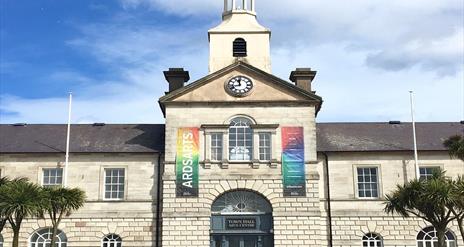 Photograph of the front exterior building of Ards Arts Centre previously the Town Hall, with backdrop of blue sky and two banners flanking the front w