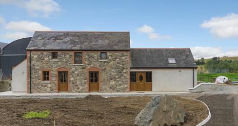 Image shows front of stone built property plus extension