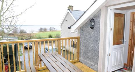 A decked entrance to a second story loft cottage with a picnic table and a view of a lake.