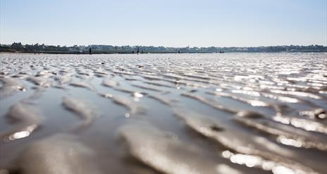 Close up photo of the ripples of sand on Ballyholme Beach with the promenade and bathers in backdrop