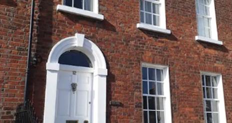 Image shows outside of property which is built in Georgian style with a white front door and sash windows. There are 2 small steps up to front door.