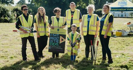 A group pic of 7 Attendees from last year's bogging event holding a sign saying I got mucky in the Bog.