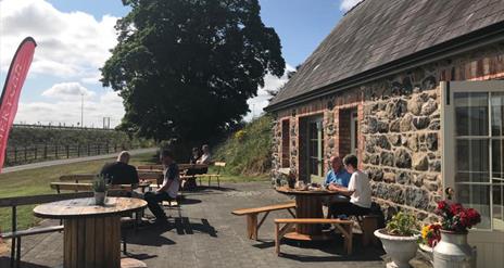 Stone cottage with people dining outside at picnic tables.