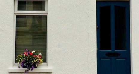 The front of a house with a dark blue door and a window decorated with flowers.