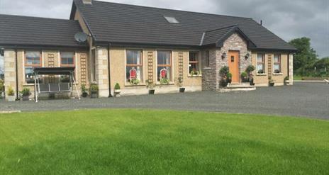 outside view of cottage with swing chair and grass garden area in image