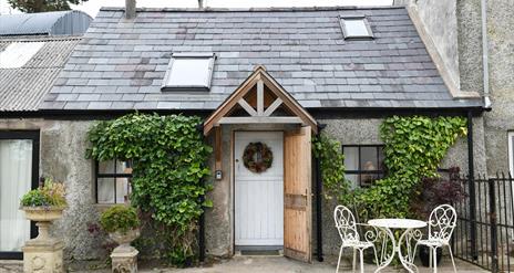 Outside view of Milk House with greenery on the walls and outside table and 2 chairs