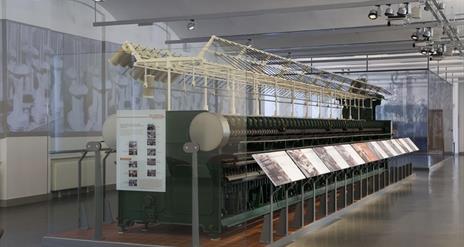 A large old spinning frame exhibit behind glass with information displays.