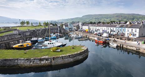 Aerial view of Carnlough Harbour with shops and homes in the background and boats in the harbour