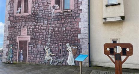 Medieval wall mural in Carrickfergus, with stocks beside it.