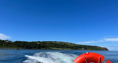 View of Blackhead path and Lighthouse with wake of sea behind boat and life ring visible on Charter NI Boat