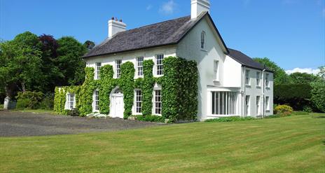 A large white house covered with decorative ivy and a freshly cut lawn.