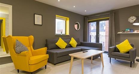 A grey sitting room with grey and yellow chairs, a grey sofa and a coffee table.