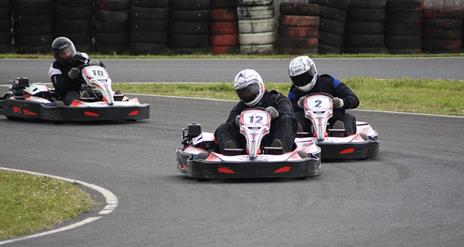 Three racers carefully turn a corner in their go-karts.