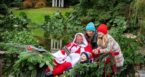 Three children are laughing and sitting with Santa in his sleigh on the grounds of Hillsborough Castle and Gardens. Santa is in a red suit.