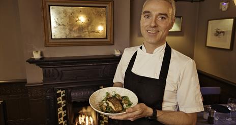 Chef holding a plate of food in front of an open fire