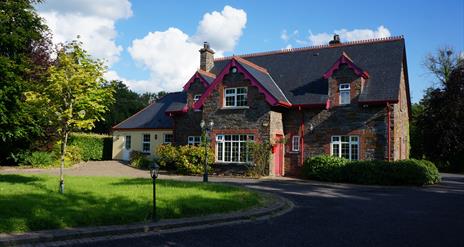 Rossclare Lodge front view of the house. A large lawn area in front of a large house in Donegal stone and a smaller painted extension to the left. A d