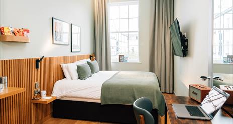 Image shows a double bed in a hotel room with paintings of Northern Ireland on the background wall