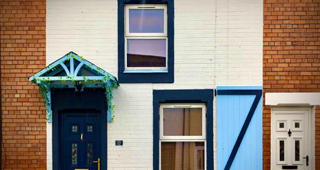 A painted terrace house designed with a light blue window shutter and canopy.