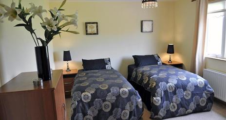 Twin bedroom with 2 single beds with bedside lockers and bunch of flowers in image