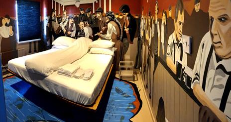 A photo of a Titanic-themed bedroom with murals of passengers on the ship, surrounding a double bed.