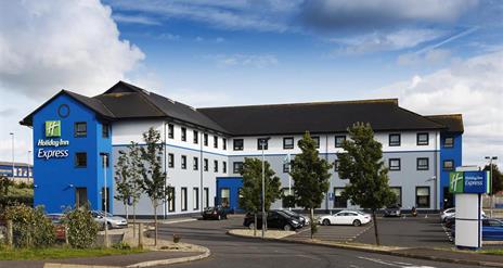 A large blue three floor hotel with a car park.