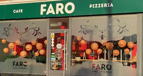 Large windows with FARO branding and green signage - Exterior shop frontage of Faro Cafe & Pizzeria at Halloween