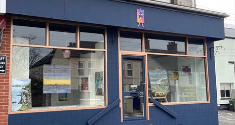 Exterior of the Gallery in Whitehead, painted blue with large windows and art displayed in them