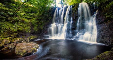 Water flowing over the rocks in Glenariff Forest with green trees surrounding the pool of water
