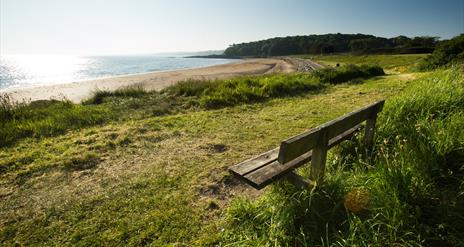 An image of Helen's Bay beach from the shore with a bench ready to welcome someone to sit