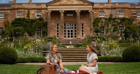 Image is of 2 girls sitting on the lawn at Hillsborough Castle