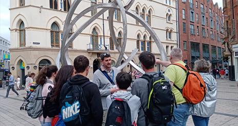 A tour group listening to a guide at a sculpture in Belfast city centre.