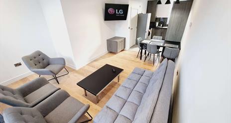 Living room with a suite, coffee table and tv leading to a kitchen with dining area and fridge.