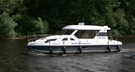 image of cruise boat in water with river bank and tress in the background.