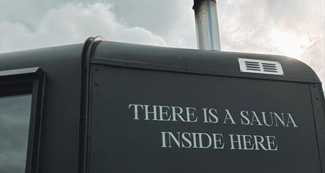 Side of matte black sauna with writing reading "there is a sauna inside here"