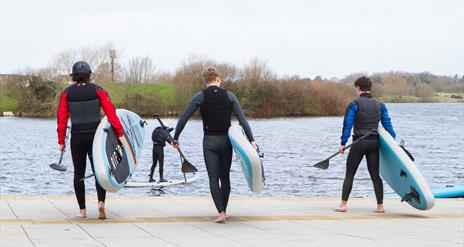 image of 3 males heading towards the lake carrying SUP paddle boards