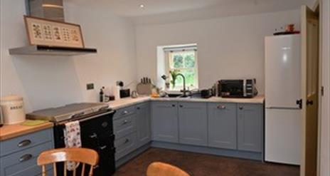 A kitchen with an antique style cooker, sink, microwave and fridge with a window.