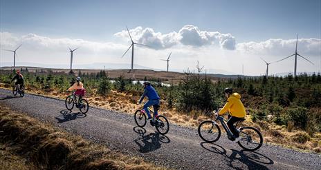 Group in single file on electric bikes on a trail with wind turbines in the background enjoying the Electric Escape experience with Corralea Adventure