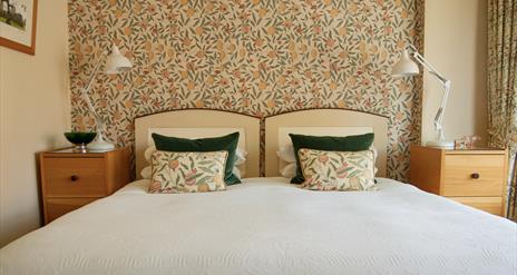 Image of a bed with patterned wall paper and matching cushions.