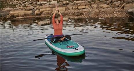 A person sitting in a yoga pose on a SUP board on water