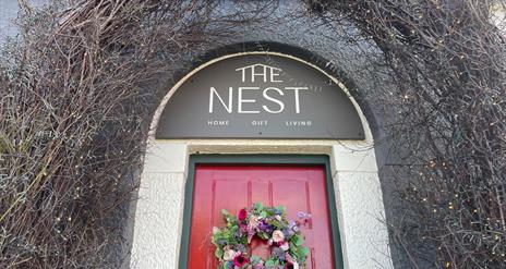 Archway over red door with sign reading The Nest and garland on the door