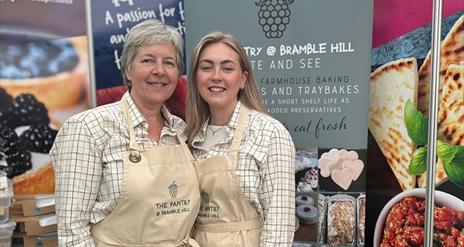 Gail from The Pantry at Bramble Hill at Balmoral Show standing in front of a display stand with a branded apron and another demonstrator
