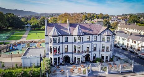 Beautiful exterior of Whistledown Hotel with blue skies, play park to the left and Warrenpoint Band Stand in the distance.