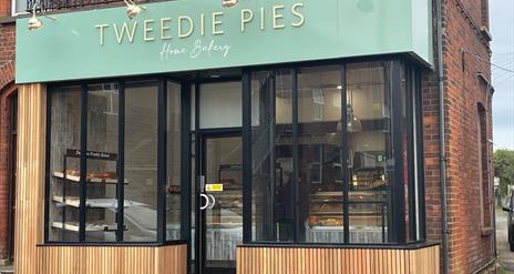 Exterior of Tweedie Pies Home Bakery with black framed glass, mint green sign and wooden panel trim
